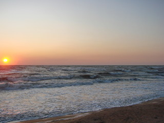 Morning storm waves of the Azov Sea covered with foam against the background of rainbow colors of sunrise.