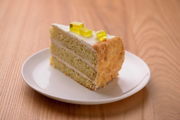 Lemon multi layered cake decorated with citron jelly and mint served on white plate on wooden background.