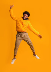 Fototapeta na wymiar Joyful black man in winter jacket happily jumping up