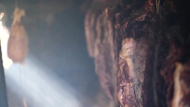 Ham and bacon hanging and drying in smokehouse on traditional way on blue smoke.  The sunrays pierce through the blue smoke.