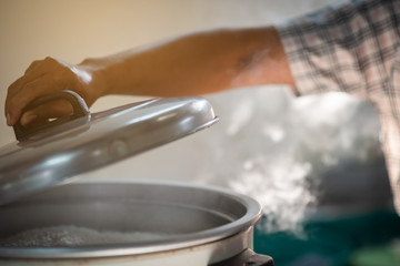 The chef's hand is opening the lid of the rice cooker, the mass of steam reflected in the morning light coming out of a large electric rice cooker heated in the cafeteria.