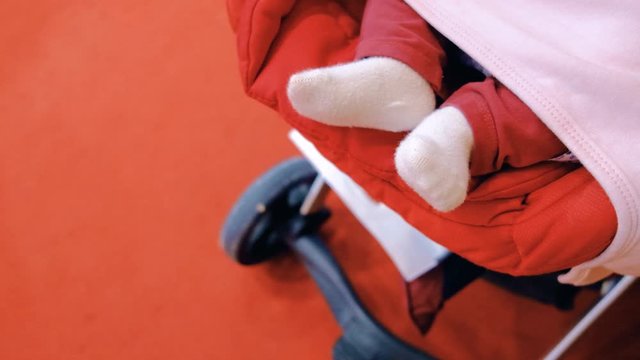Newborn baby swinging her feet while sleeping in a stroller, top view