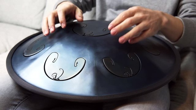 Close up of man hands playing hang drum indoors. Unusual music instrument. Concept of sound for meditation