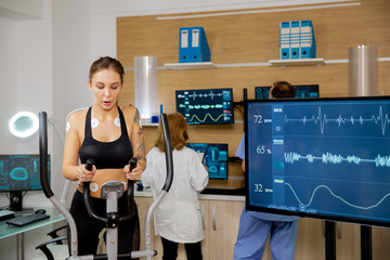 Female athlete who makes a physical effort on the stepper and has electrodes attached to it and her...