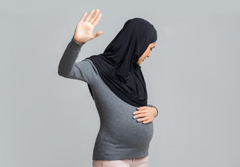 Scared pregnant muslim woman in hijab doing stop gesture, hiding face