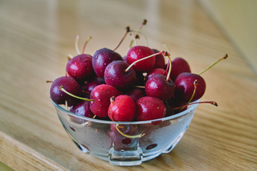 Fresh cherry glass bowl ready to serve. On a light-coloured wooden background, perfect for adding text
