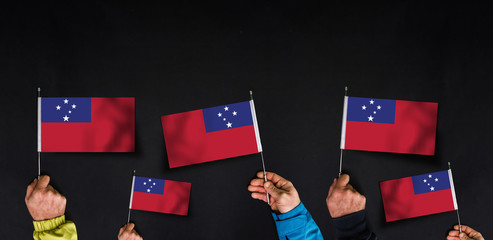 Hands holds flags of Samoa on dark background