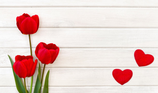 Decoration of Valentine Day. Beautiful red tulips and red hearts on background of white painted wooden planks with space for text. Top view, flat lay