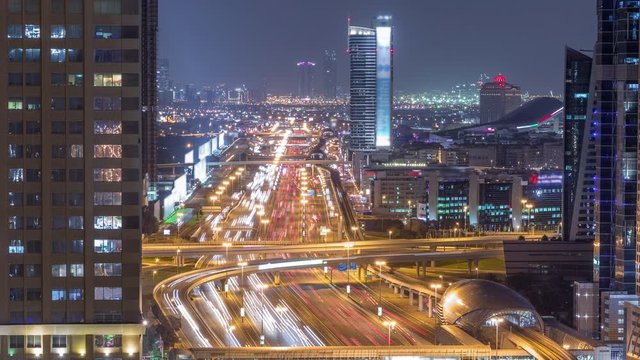 Skyline internet city with crossing Sheikh Zayed Road aerial night timelapse. Illuminated skyscrapers with traffic on a highway and metro line in Dubai