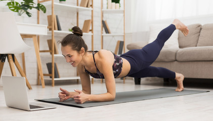 Fit woman doing yoga plank and watching online tutorials on laptop