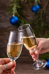Glasses of champagne with bubbles on the background of Christmas decorations. Glasses in the hands of people touch during a festive toast. Beautiful card.