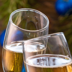 Glasses of champagne with bubbles on the background of Christmas decorations. Glasses in the hands of people touch during a festive toast. Beautiful card. Square.