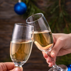 Glasses of champagne with bubbles on the background of Christmas decorations. Glasses in the hands of people touch during a festive toast. Beautiful card. Square.