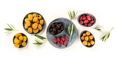 Olives flat lay panorama on a white background, top shot. Black, green and red olives of various sizes, with leaves