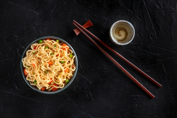 Instant noodles with vegetables, with sake and chopsticks, shot from the top on a dark background...