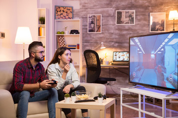 Man sitting on sofa next to his girlfriend and playing video games