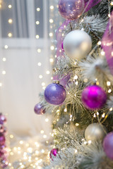Close up of Christmas tree branches with purple decorative baubles and bokeh lights on background. New Year garlands. Copy space, vertical shot. 