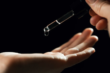 skin care and treatment - woman drops oil in a hand with pipette on black background