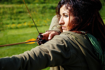 detail of a woman training shooting with a bow on a meadow,