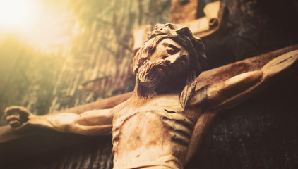 Antique wooden statue of crucified Jesus Christ against dark wooden background