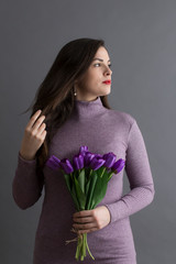 Medium profile portrait of beautiful dreamy young brunette in long mauve turtleneck holding a bouquet of silk tulips and touching her long hair