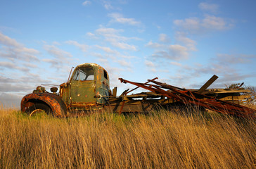 Old truck abandoned in a field of waving grass beneath a cloudy blue sky.