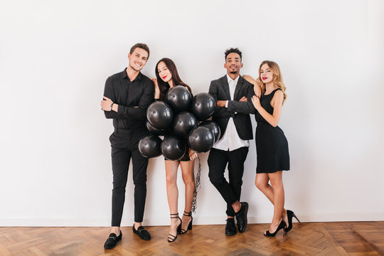 Full-length portrait of girls and boys with party balloons preparing house for event. Indoor photo of two loving couples posing on white background after double date.