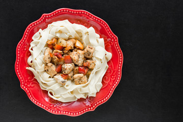 Spaghetti with stew chicken and vegetables on red plate on black background with copy space