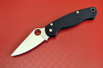 Military folding knife stainless steel sharp blade black handle red background