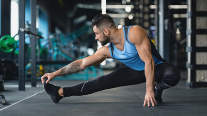 Fototapeta na wymiar Young athlete stretching legs before training at gym