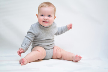  A 6 month old baby learns to sit down. photo on a neutral background