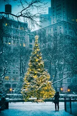 Plexiglas foto achterwand Snow-covered Christmas tree with golden lights glowing against a stark urban background after a winter blizzard in New York City © lazyllama