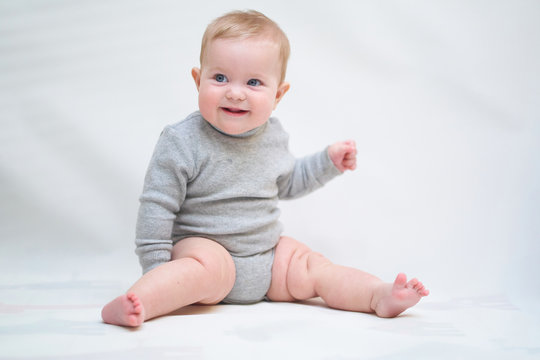  A 6 month old baby learns to sit down. photo on a neutral background