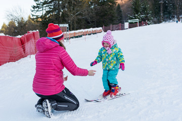Active mother teaching her daughter to ski.