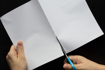 Woman hands cutting rectangular sheet of paper in half on the black background