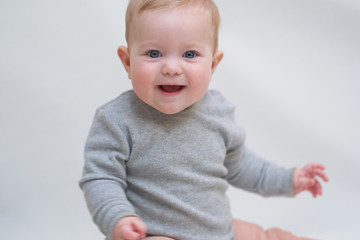  A 6 month old baby learns to sit down. photo on a neutral background