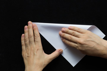 Naklejka premium Woman hands folding rectangular sheet of paper to make it square on the black background