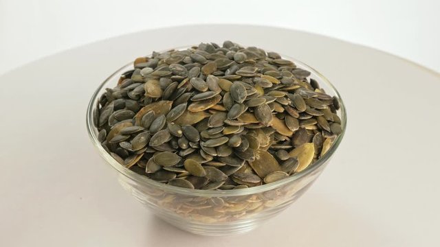 Nuts peeled pumpkin seed rotate are on a table in a plate. Snack in transparent dish on an isolated white background are spinning moving. Delicious and healthy protein-rich diet food.