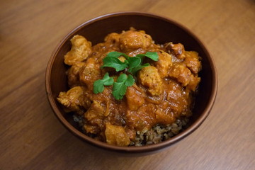 Soy meat stewed in tomato sauce with buckwheat in a ceramic brown bowl on a wooden table close-up. Green parsley and arugula on the top. Selective focus