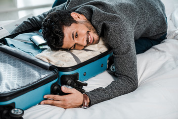 handsome and smiling bi-racial man lying on travel bag