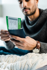 cropped view of bi-racial man in sweater holding passport with air ticket