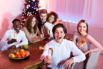 Friends Holding Glasses Sitting At Table Having Christmas Home Party