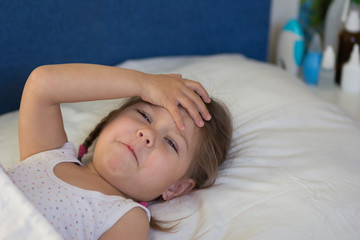 Fototapeta na wymiar Caucasian sad unhealthy child of three age lying in bed holding her hand on head looking at camera