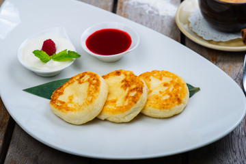 Traditional breakfast with coffee and cheesecakes, cottage cheese pancakes on a plate with syrup and jam.