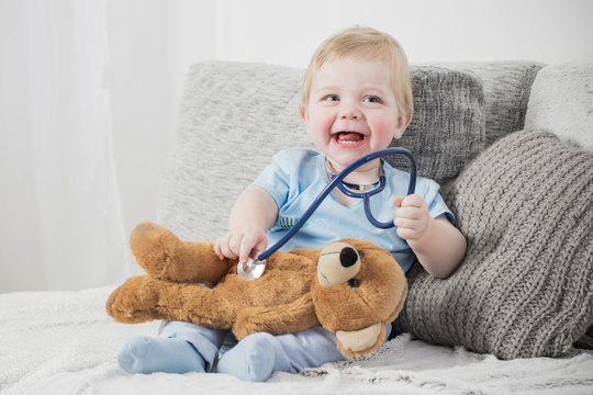 Little Child Plays Doctor With Teddy Bear At Home