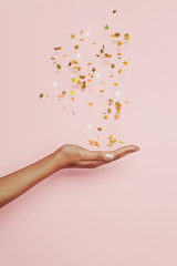 Blowing confetti stars decor in woman hand on pink background. Holiday, fantasy and imagination...