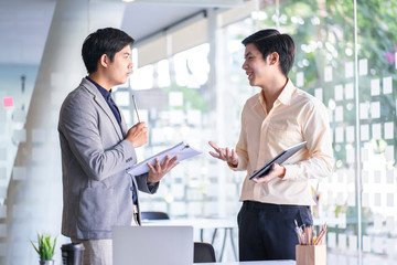 Young Asian businessmen using a digital tablet to discuss information in a modern business working space.