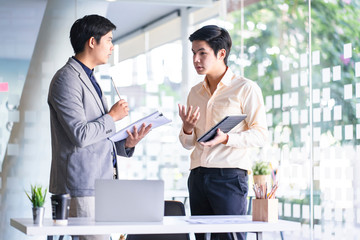 Fototapeta premium Young Asian businessmen using a digital tablet to discuss information in a modern business working space.