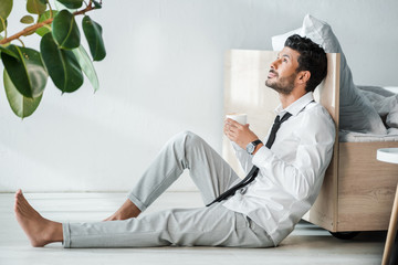 side view of handsome bi-racial businessman holding cup of coffee in morning