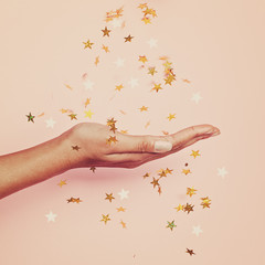 Magical gold confetti stars decoration in female hand on pastel pink background